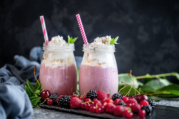 Dois frascos de milk-shake ou batido com cranberries, morangos e mirtilos em pé na superfície da pedra