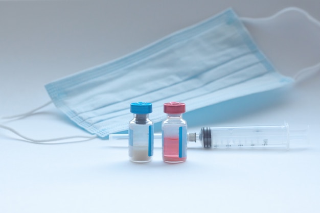 Dois frascos de vacina estão brancos com uma máscara médica e uma seringa
