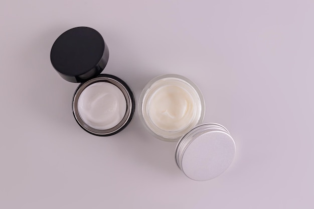 Foto dois frascos de vidro com um creme cosmético natural para o cuidado da pele anti-envelhecimento do rosto e do corpo creme diurno e noturno em frascos abertos