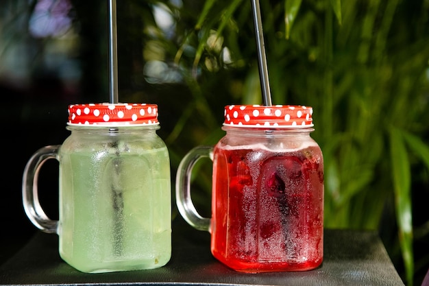 Dois frascos de vidro de coquetéis vermelhos e verdes com canudos sobre uma mesa.