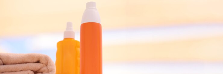 Foto dois frascos laranja com protetor solar na praia perto de toalhas.