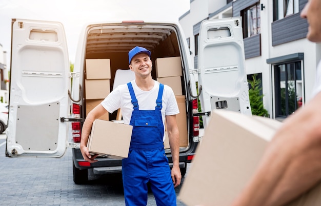 Dois funcionários da empresa de mudanças descarregando caixas do microônibus para a casa dos clientes