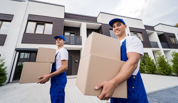 Dois funcionários da empresa de mudanças descarregando caixas na casa de novos clientes