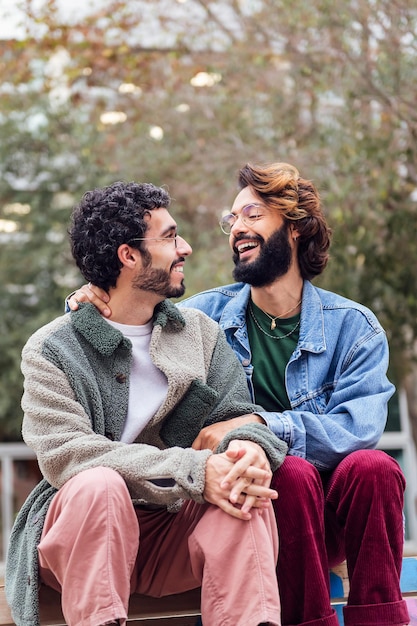 Dois gays sentados em um parque sorrindo felizes