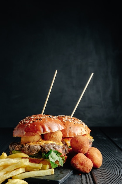 dois grandes hambúrgueres suculentos com batatas fritas, bolas de queijo em uma parede preta