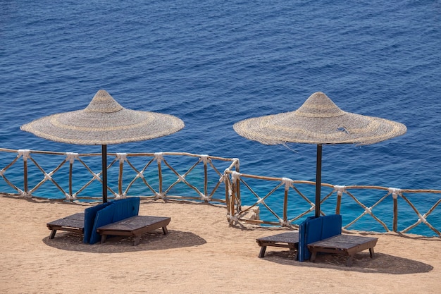 Dois guarda-chuvas de palha com espreguiçadeiras de madeira ao lado do mar vermelho na praia de areia no resort em Sharm El Sheikh Egito