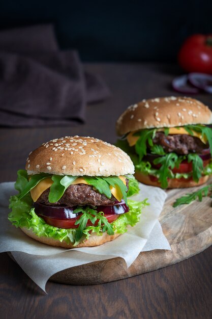 Dois hambúrgueres feitos de carne bovina, queijo de alface e pão fatiado, servidos em uma mesa de madeira escura