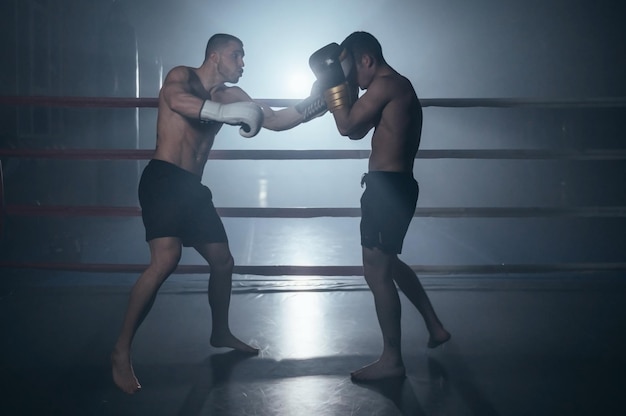 Dois homem musculoso sem camisa lutando kick boxing no ringue de boxe