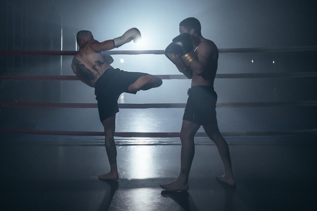 Dois homem musculoso sem camisa lutando kick boxing no ringue de boxe