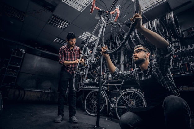 Dois homens atraentes estão trabalhando na fixação de bicicletas na oficina escura.