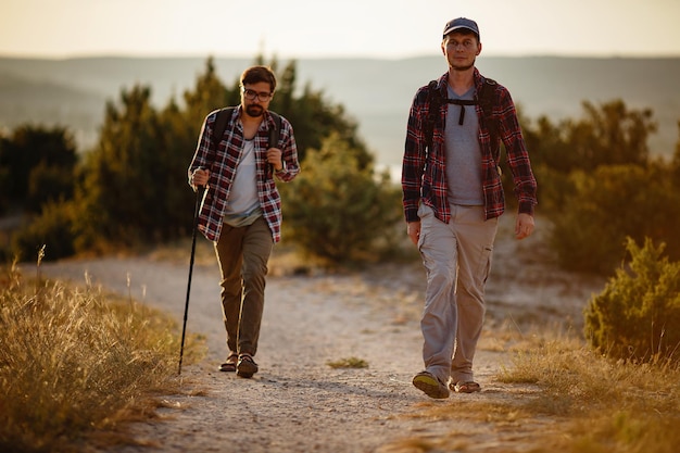 Dois homens caminhantes desfrutam de um passeio na natureza ao pôr do sol no verão