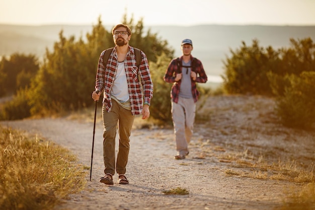Dois homens caminhantes desfrutam de um passeio na natureza ao pôr do sol no verão