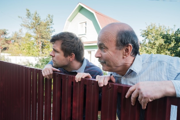 Dois homens caucasianos cuidadosamente observando por cima da cerca