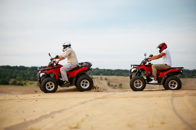 Foto dois homens com capacetes, atv cavalgando nas areias do deserto