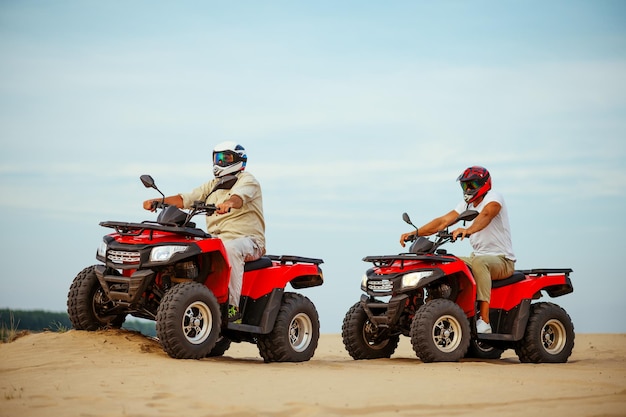 Dois homens com capacetes, um atv da liberdade cavalgando nas areias do deserto. homens em quadriciclos, corrida na areia, safári nas dunas em um dia ensolarado, 4x4 aventura extrema, conceito de quadriciclo