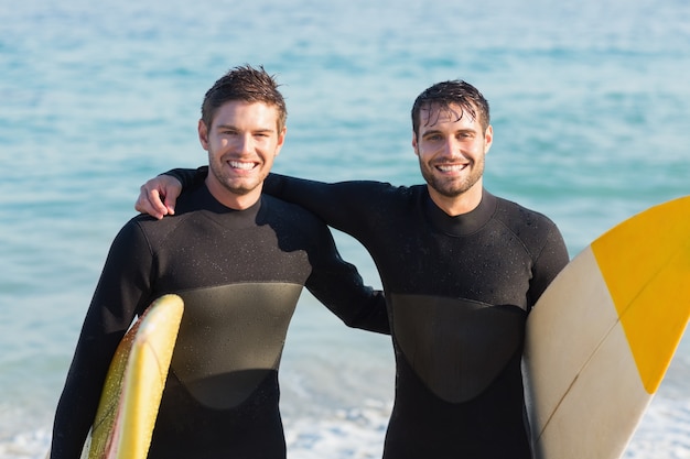 Dois homens com roupa de mergulho com prancha em um dia ensolarado