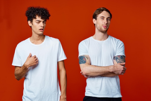 Dois homens de camiseta branca ao lado do fundo vermelho de comunicação