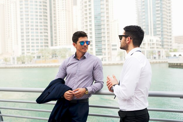 Dois homens de negócios elegantes e atraentes se inclinaram em cima do muro para conversar.