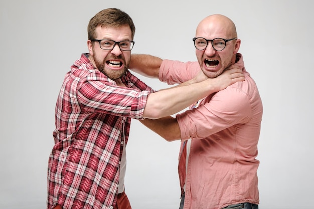 Dois homens de óculos se estrangulam, olham furiosamente para a câmera