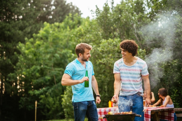 Dois homens desfrutando de cerveja e fazendo churrasco juntos