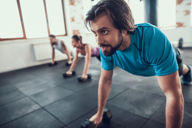 Dois homens e mulher fazendo push ups em halteres.