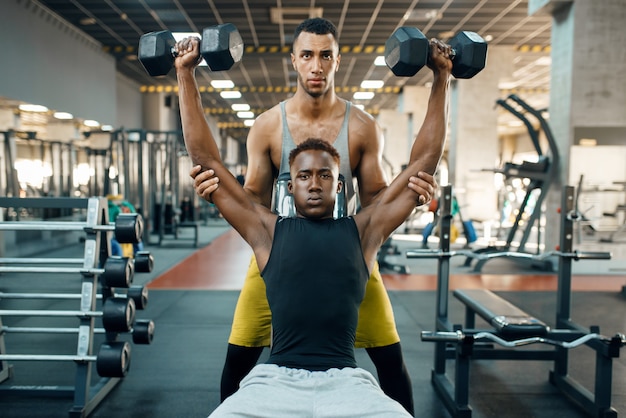 Dois homens fazendo exercícios com halteres no banco, treinando na academia