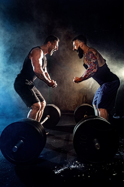 Dois homens musculosos tatuados barbudos se olham e gritam na academia