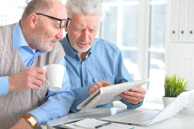 Dois homens sênior sentados à mesa e lendo jornal