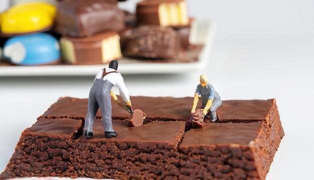 Dois homens trabalhando em um brownie com um prato de comida ao fundo.