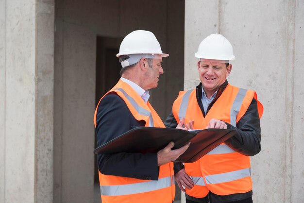 Dois homens vestindo coletes de segurança conversando no canteiro de obras