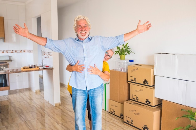 Foto dois idosos alegres, felizes com a nova casa para um novo começo, como aposentados com caixas móveis no chão - luz forte da janela