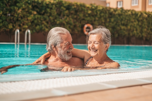 Dois idosos felizes, se divertindo e curtindo juntos na piscina, sorrindo e brincando. pessoas felizes curtindo o verão ao ar livre na água