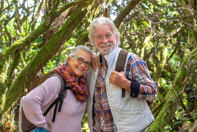 Dois idosos, homem e mulher, desfrutando de caminhada na montanha na floresta entre troncos e galhos cobertos de musgo durante a temporada de outono conceito de diversão e idosos aposentados ativos
