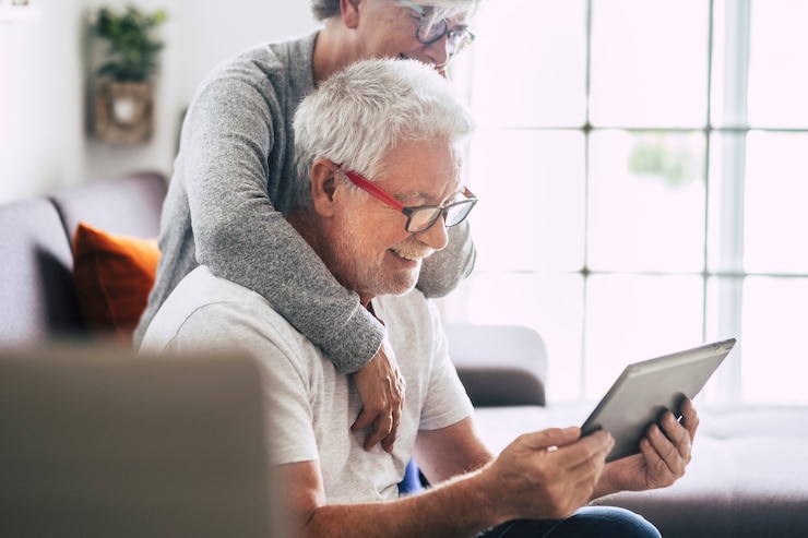 Foto dois idosos sorrindo e olhando para o tablet - mulher monopolizando o homem com amor no sofá - interior