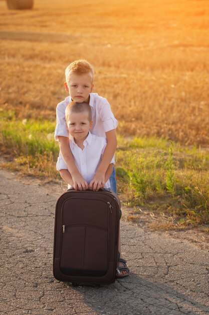 Dois irmãos com uma mala na estrada no verão ao pôr do sol