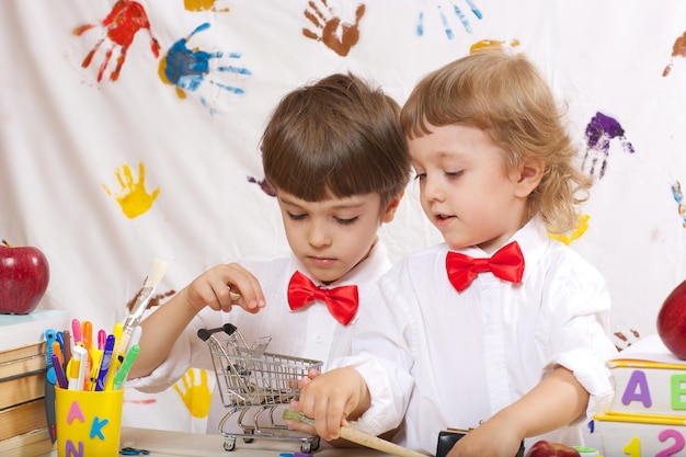 Foto dois irmãos de 7 e 4 anos vestidos com camisas brancas com lacinhos vermelhos estão jogando juntos.