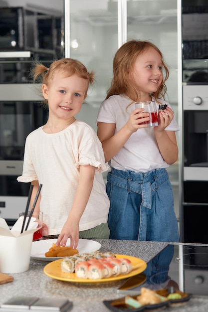 Dois irmãos de meninas se divertindo e comendo na cozinha em casa com comida japonesa