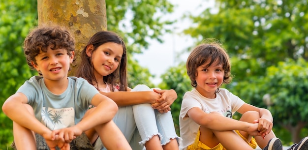 Dois irmãos e uma irmã sorrindo em um parque ao lado de uma árvore