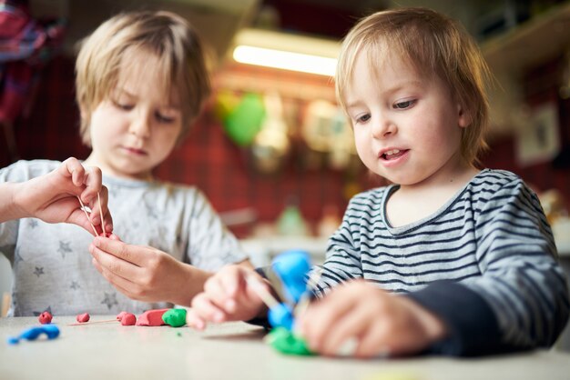 Dois irmãos fazem figuras tridimensionais de plasticina e paus