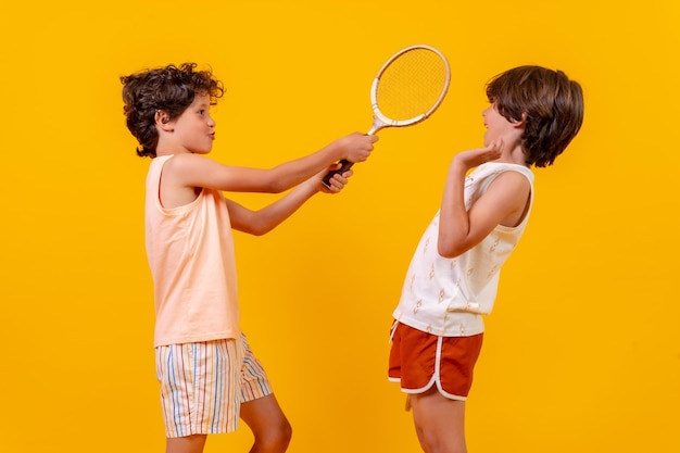 Dois irmãos jogando tênis e se divertindo no fundo amarelo de férias de verão