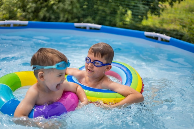 Dois irmãos meninos na piscina ao ar livre perto da casa nadam e brincam de natação colorida r...