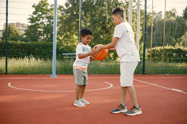 Dois irmãos multiracionais jogando basquete em uma quadra perto do parque