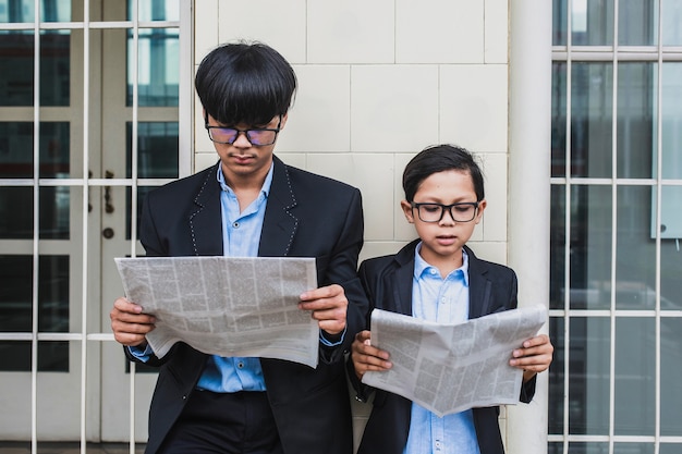 Dois irmãos usando óculos com camisa azul e paletó preto lendo jornal