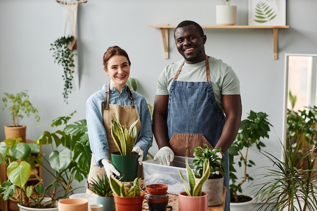 Dois jardineiros sorridentes olhando para a câmera dentro de casa posando com plantas verdes