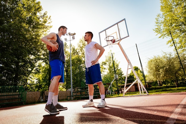 Dois jogadores de basquete negociando antes de treinar ao ar livre. eles estão de pé na quadra e conversando.