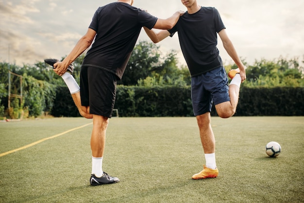 Dois jogadores de futebol fazendo exercícios de alongamento no campo.  treinamento de futebol em estádio ao ar livre, treino em equipe antes do  jogo