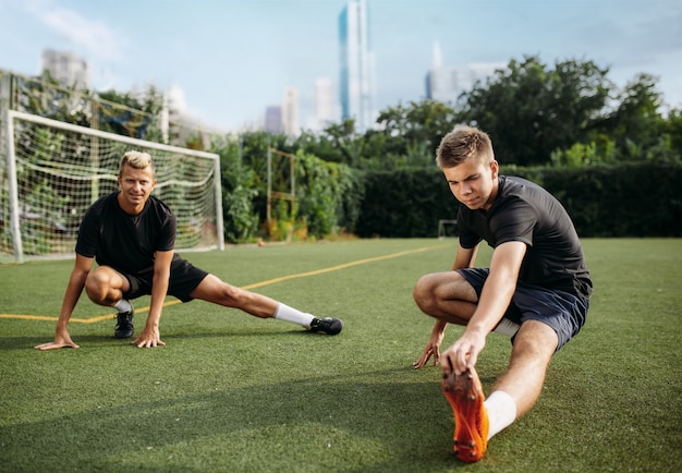 Foto dois jogadores de futebol masculino fazendo exercícios de alongamento no campo. treinamento de futebol em estádio ao ar livre, treino em equipe antes do jogo