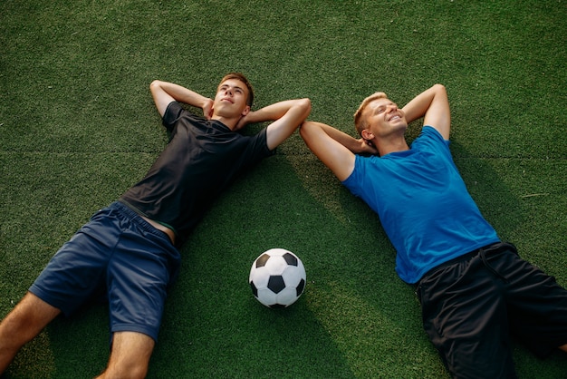 Dois jogadores de futebol masculinos deitado na grama do campo, vista  superior. jogador de futebol no estádio ao ar livre, treino antes do jogo,  treino de futebol