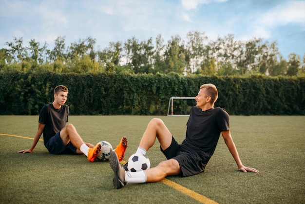 Dois jogadores de futebol masculinos descansando na grama do campo. jogadores de futebol no estádio ao ar livre, treino antes do jogo, treino de futebol