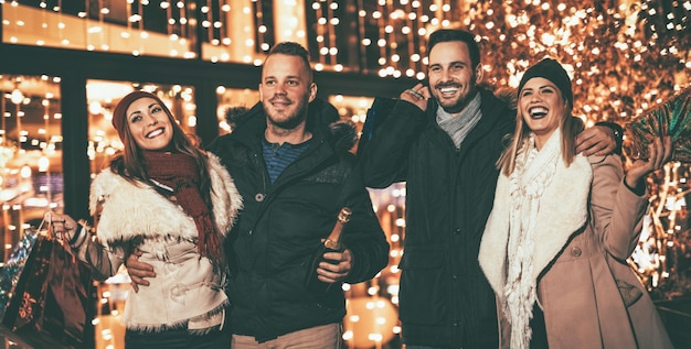 Dois jovem casal alegre se divertindo na festa de Natal ao ar livre na rua da cidade à noite e com muitas luzes no fundo.